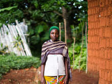 Eine Frau mit einem grünen Hut posiert für ein Foto vor einem Haus in Burundi.